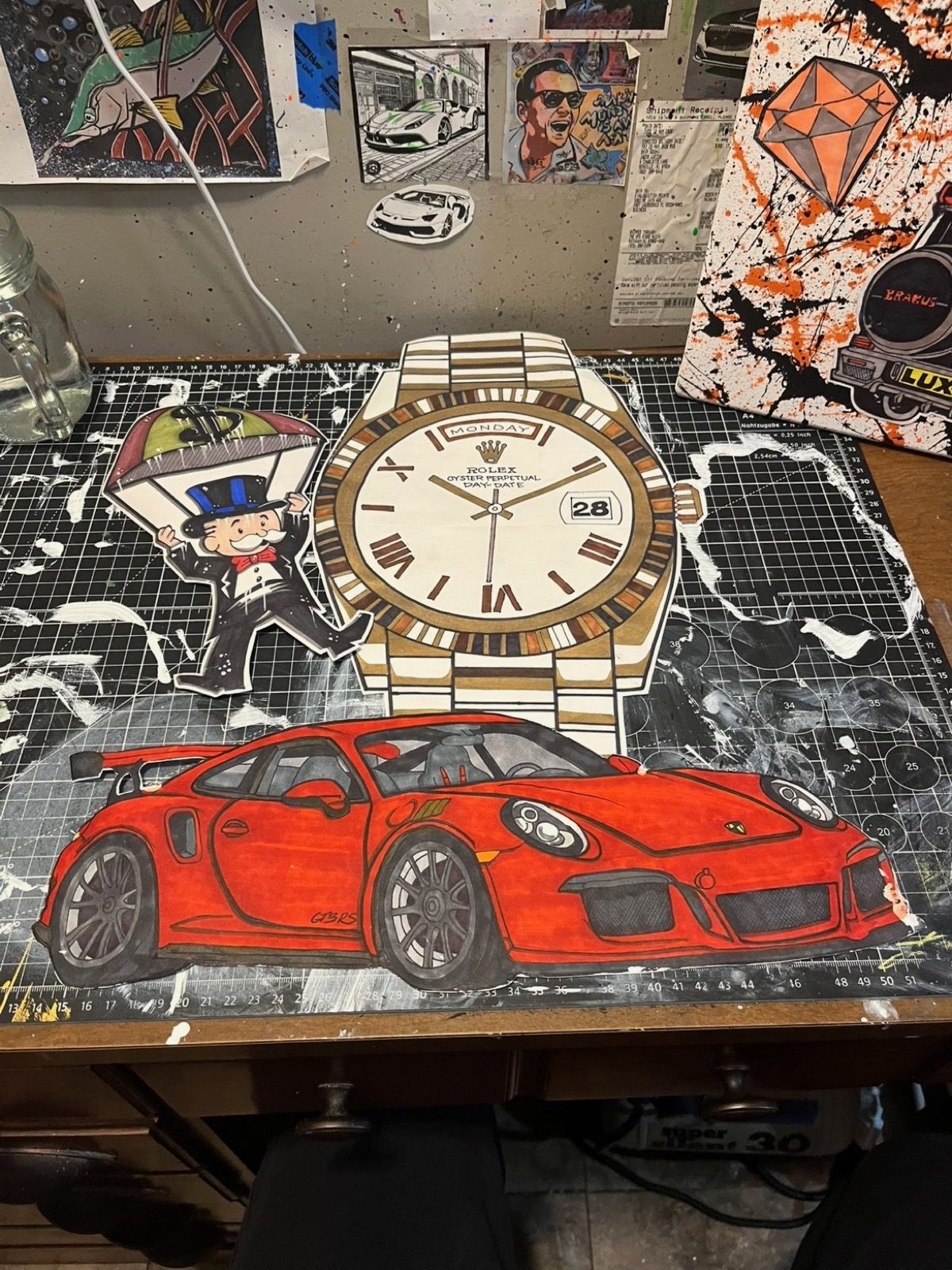 Hand-cut red sports car, gold watch and character illustrations on Jacob’s studio table